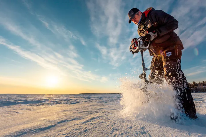 Kalastaja poraa reikää paksuun jäähän sähköporalla